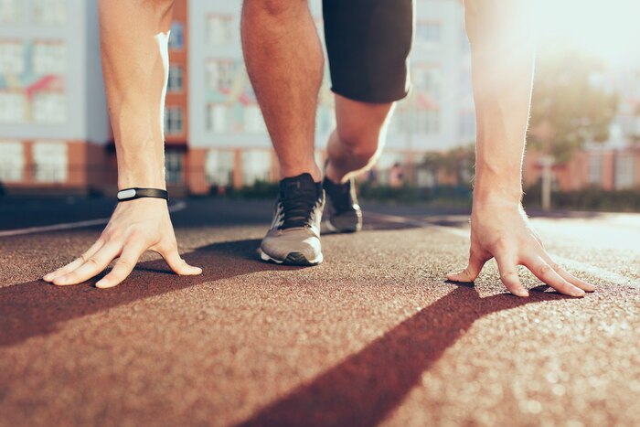 Muscle, hands, sunlight, legs in sneakers of strong guy on stadium in the morning. he has preparation on start.