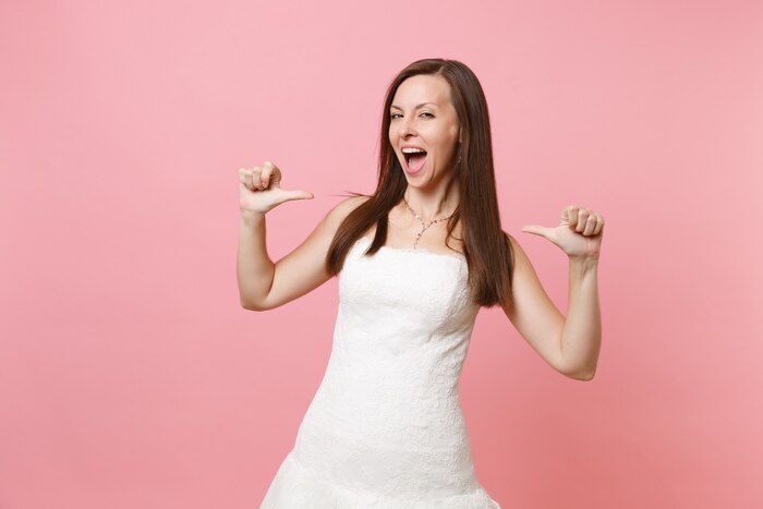 Portrait of narcissistic woman with opened mouth in elegant lace white dress pointing thumbs on herself