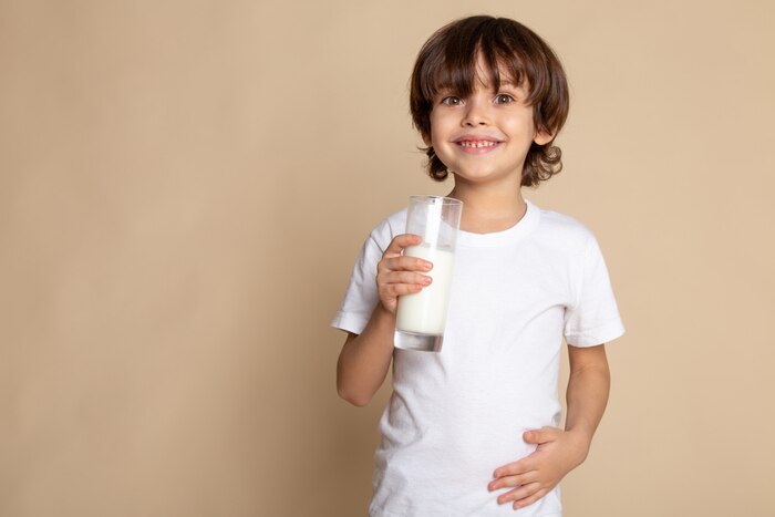 Cute boy adorable in white t-shirt drinking white whole milk on pink desk